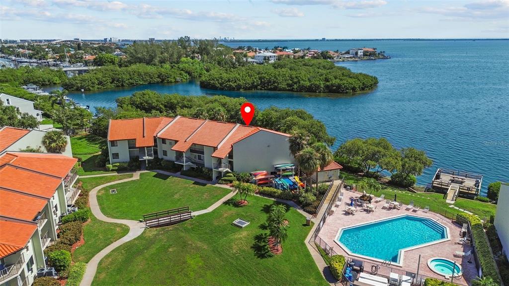 An aerial view shows a waterfront condominium complex with a pool and green lawn — 1515 PINELLAS BAYWAY S UNIT 65, ST PETERSBURG, FL