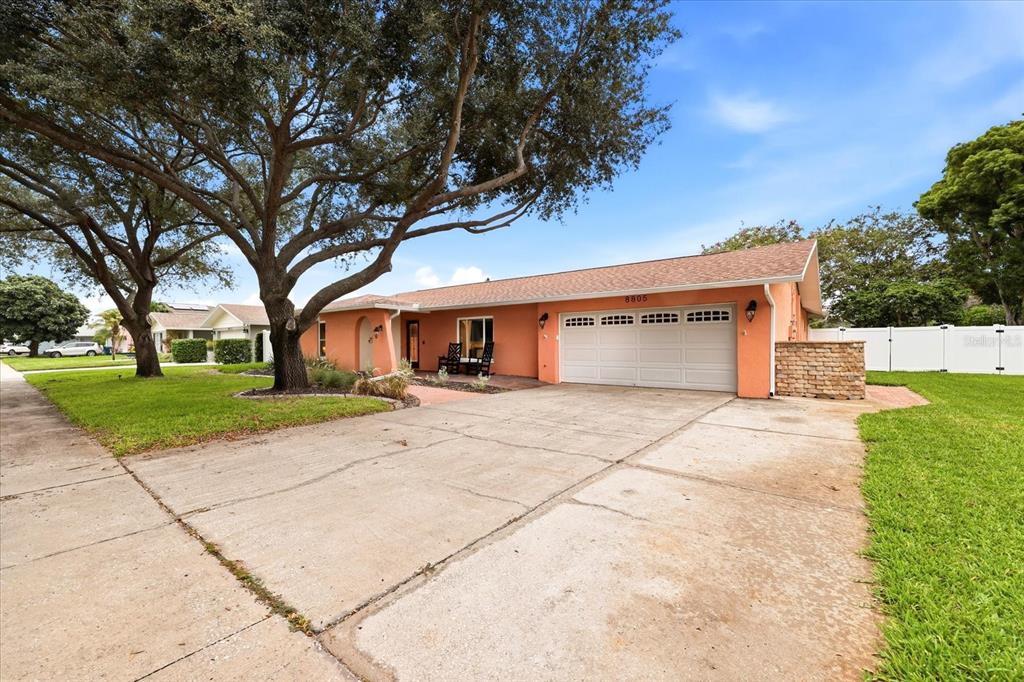 A single-story peach-colored house with a large tree, a concrete driveway, and a two-car garage — 8805 KENWOOD ROAD, SEMINOLE, FL