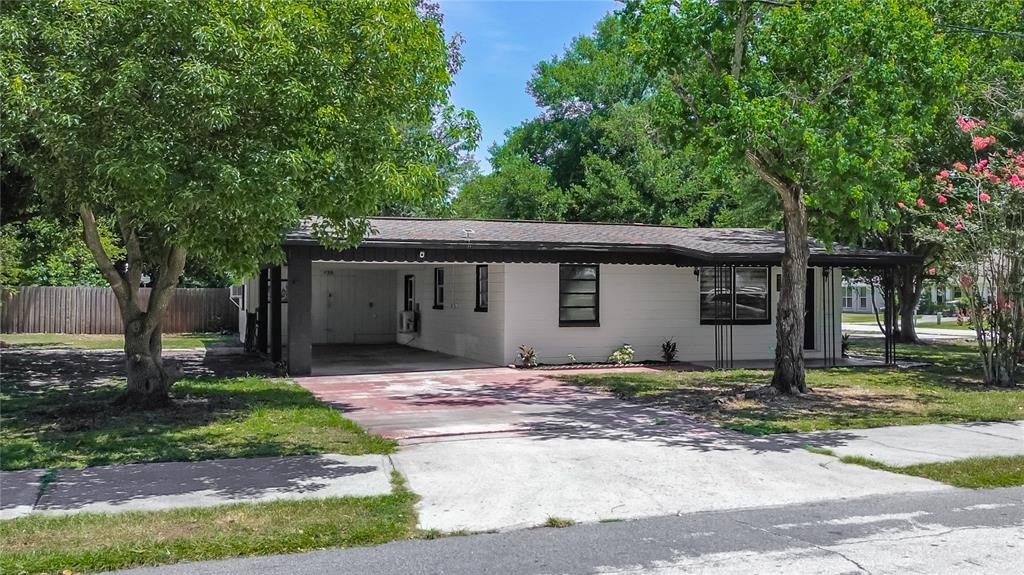 A single-story white house with a carport and a concrete driveway under mature trees — 438 CALIFORNIA AVENUE, ST CLOUD, FL