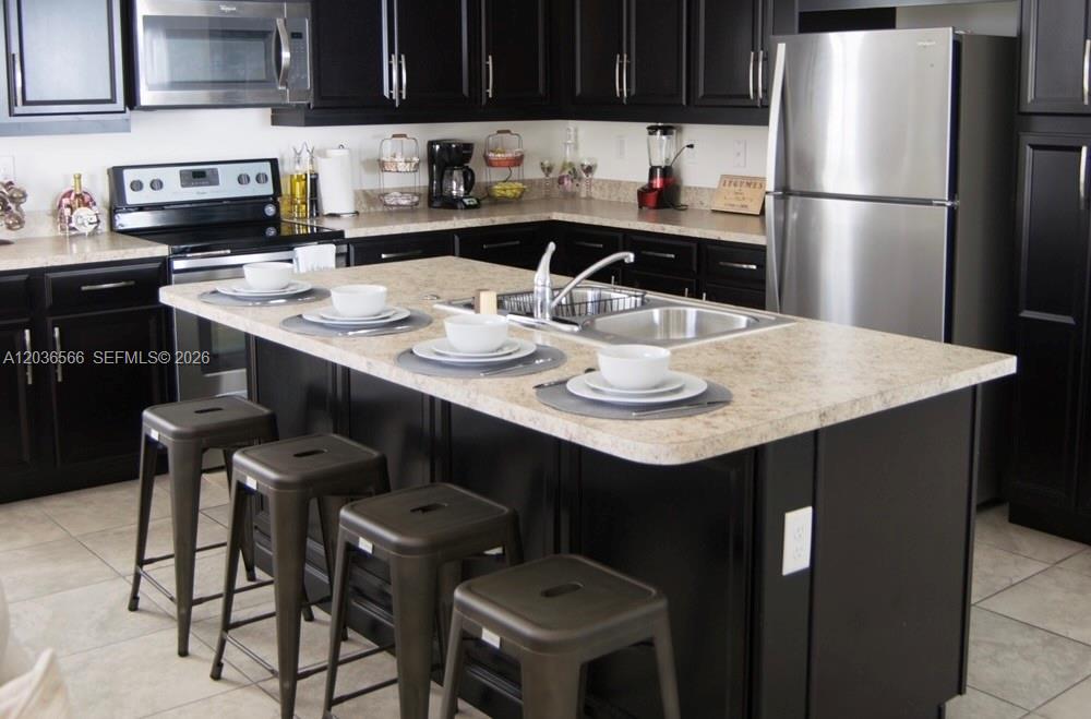 A kitchen features dark cabinetry, a beige countertop island with a sink, and stainless appliances — 14920 SW 175th St, Miami FL 33187, MIAMI, FL