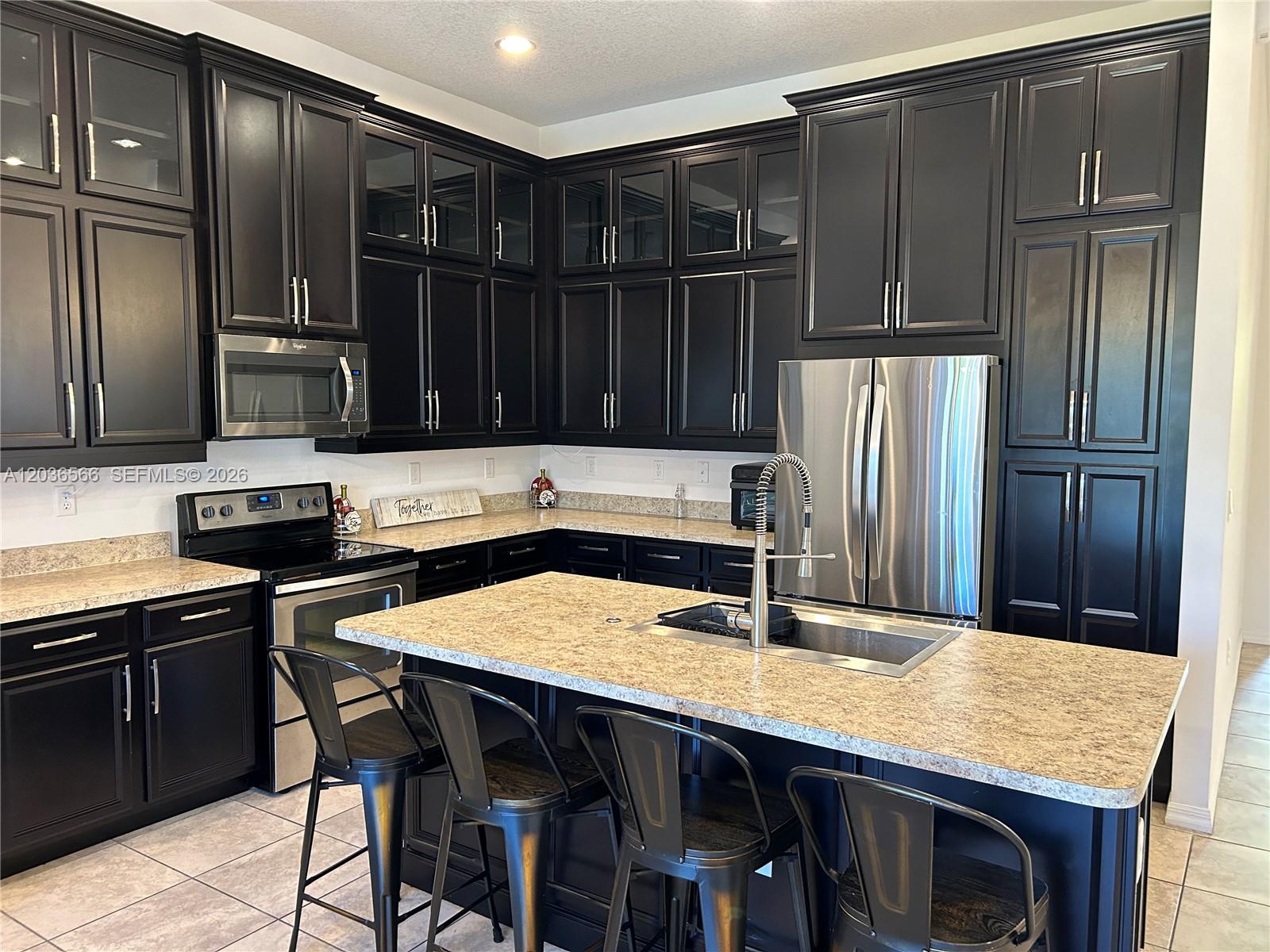 A kitchen features dark cabinetry, stainless steel appliances, a granite island, and four metal stools — 14920 SW 175th St, Miami FL 33187, MIAMI, FL