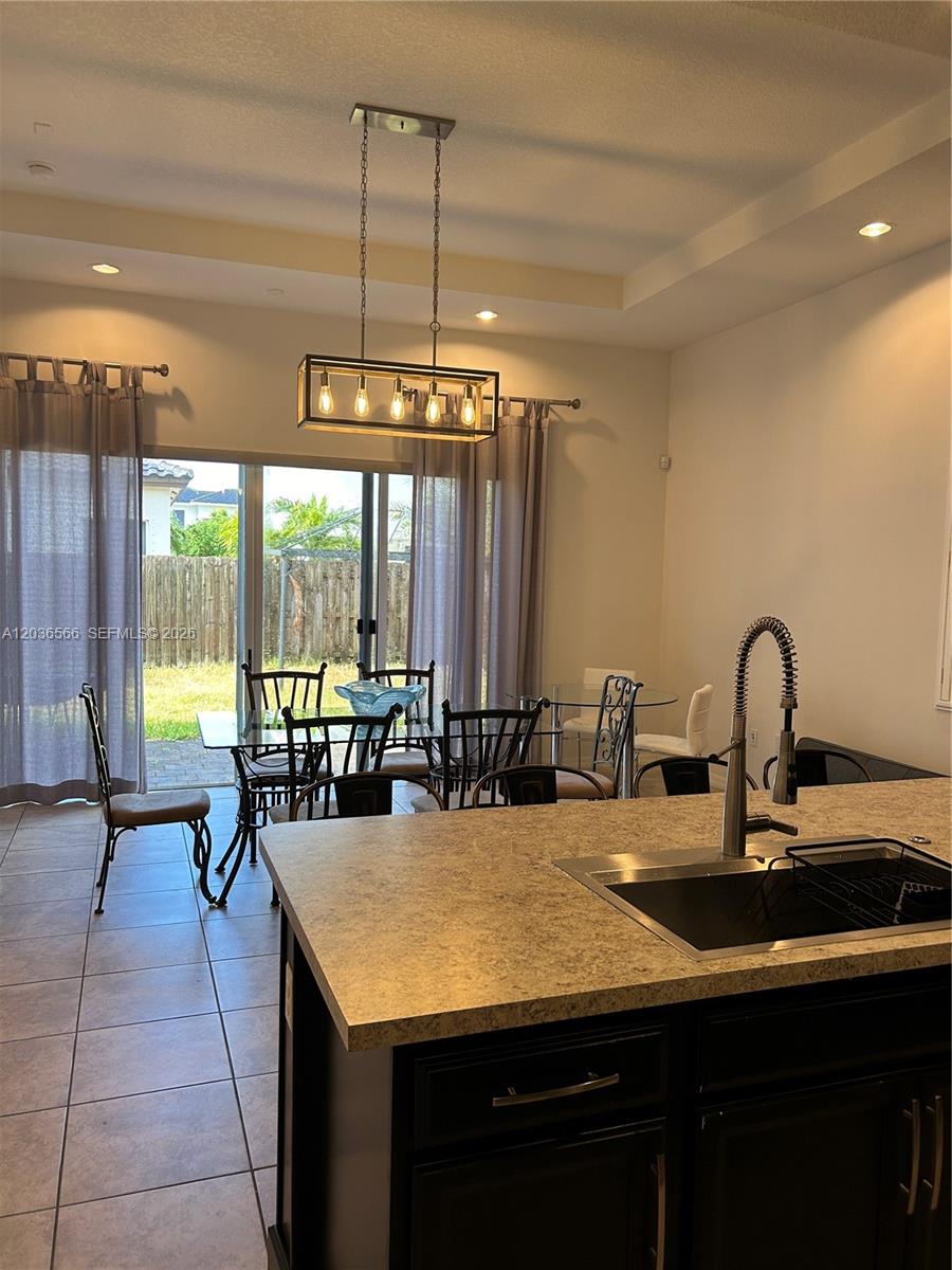 A kitchen island with a sink overlooks a dining area with a glass table — 14920 SW 175th St, Miami FL 33187, MIAMI, FL
