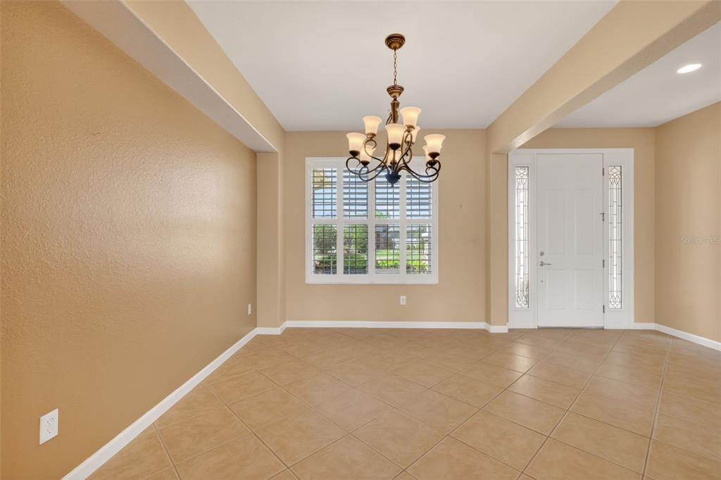 A dining room with tan walls, tile flooring, a chandelier, and a front entryway door — 9455 SW 71ST LOOP, OCALA, FL