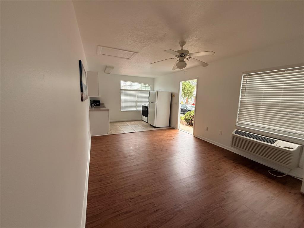 An open-concept living area with wood-look flooring leads to a kitchen with white appliances — 527 CARIBBEAN DRIVE UNIT B, DAVENPORT, FL