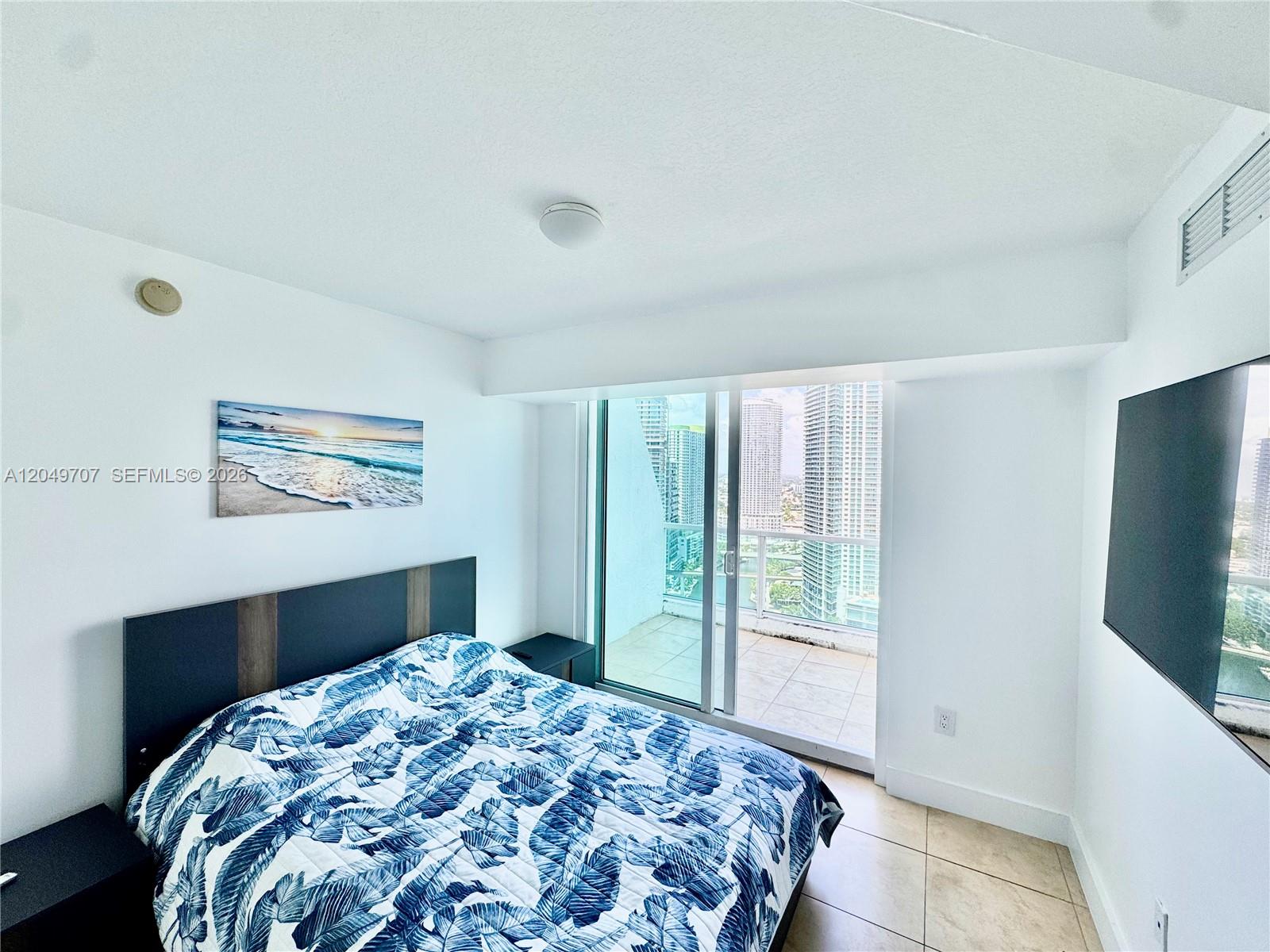 A bedroom features a bed with a leaf-patterned quilt and a balcony overlooking city skyscrapers — 41 SE 5th St # 1917, Miami FL 33131, MIAMI, FL