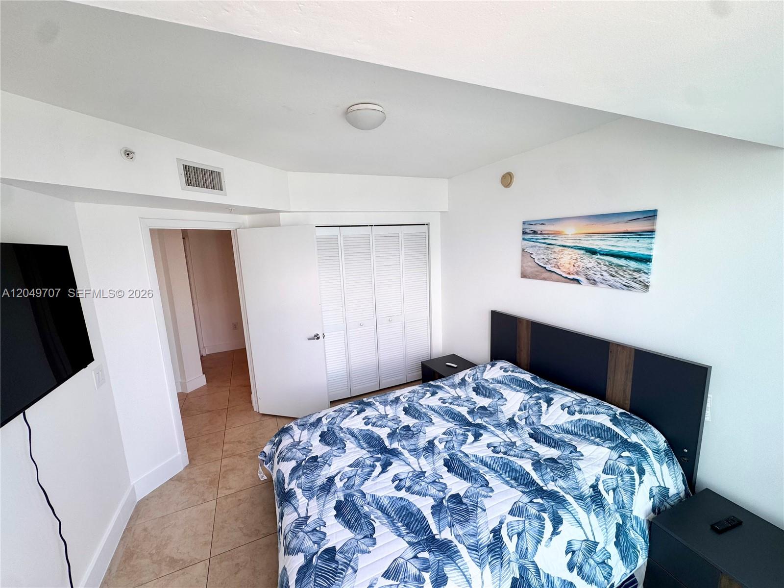 A bedroom features a bed with a blue leaf-patterned comforter and tiled flooring — 41 SE 5th St # 1917, Miami FL 33131, MIAMI, FL