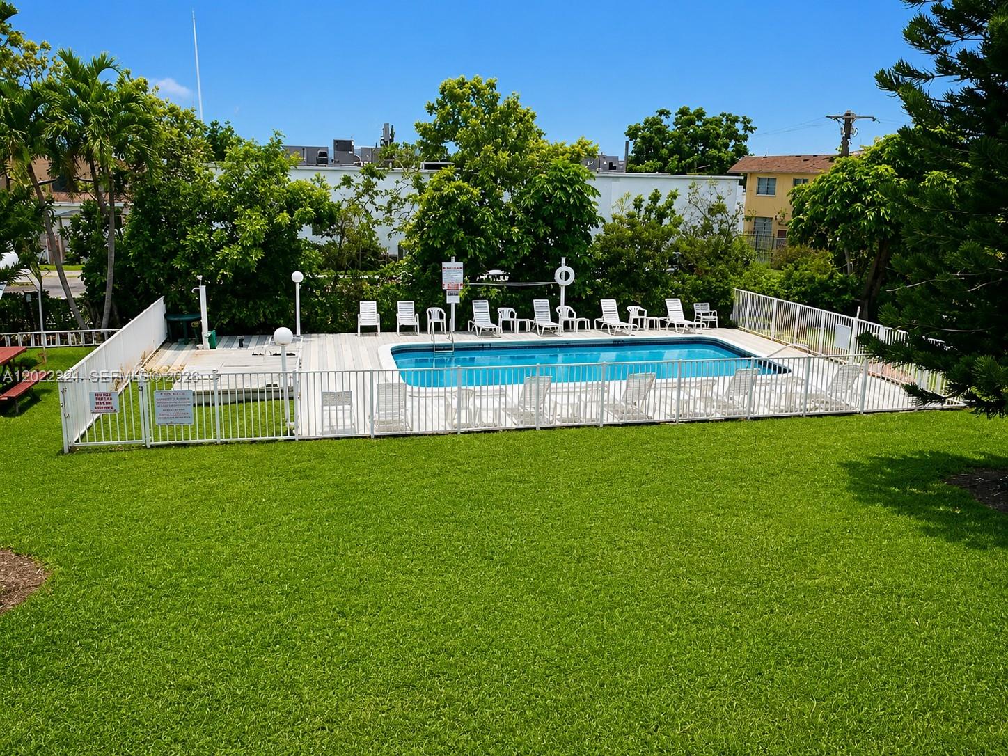 An outdoor swimming pool is surrounded by a white fence and lounge chairs on grass — 2839 Taylor St # 8, Hollywood FL 33020, HOLLYWOOD, FL