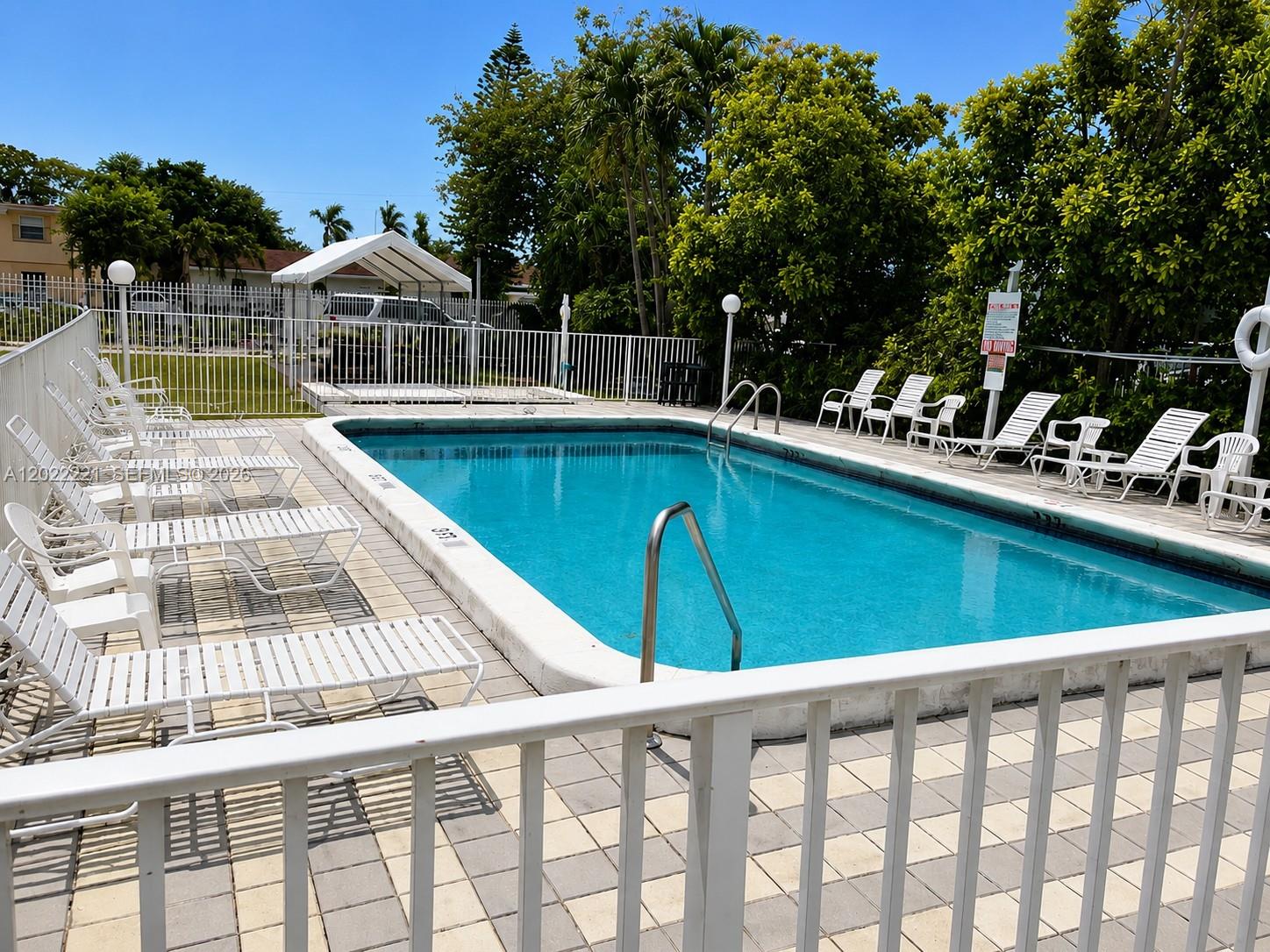 A rectangular swimming pool is surrounded by white lounge chairs and a white fence — 2839 Taylor St # 8, Hollywood FL 33020, HOLLYWOOD, FL