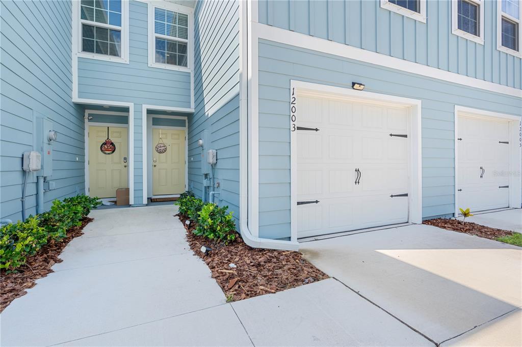 A light blue townhouse exterior features two front doors, two garage doors, and a walkway — 12003 GRIZZLY LANE, NEW PORT RICHEY, FL