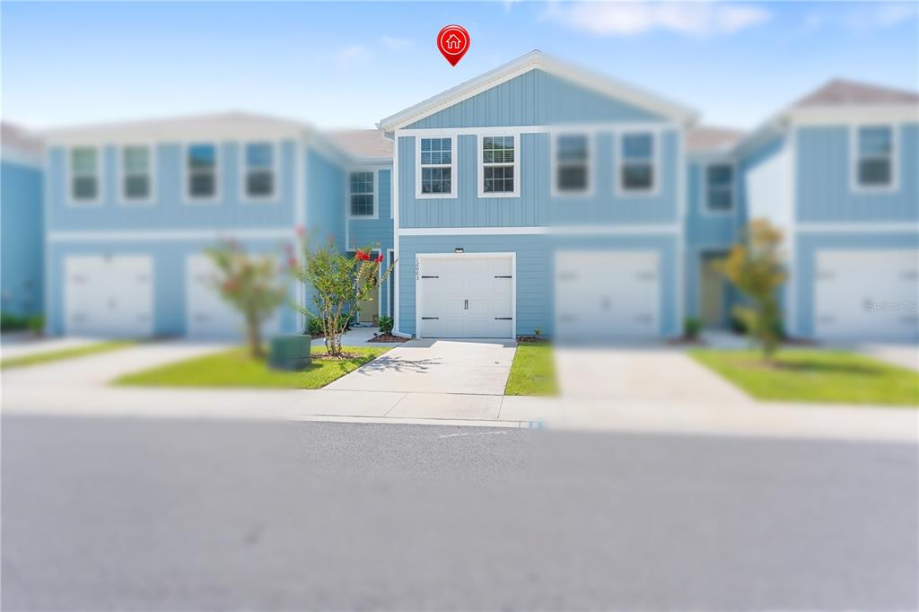 A light blue two-story townhouse features a white garage door and a concrete driveway — 12003 GRIZZLY LANE, NEW PORT RICHEY, FL