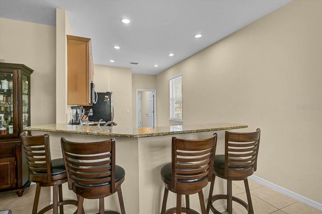 A kitchen features a granite breakfast bar with four wooden stools and recessed lighting — 9815 NOSTALGIA PLACE, ENGLEWOOD, FL