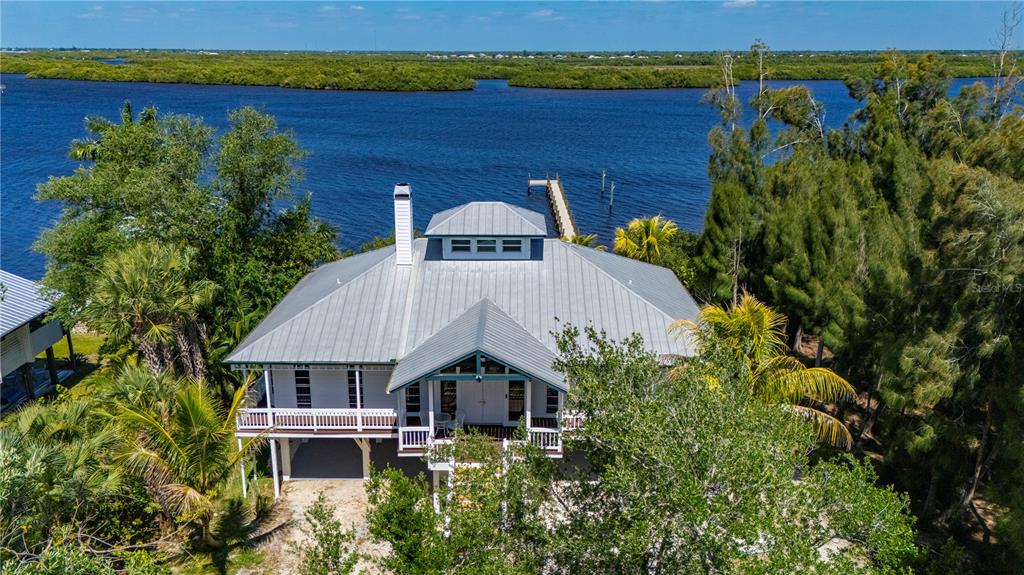 An elevated white house with a metal roof sits beside a dock on the water — 27414 MISTY AVENUE, PUNTA GORDA, FL