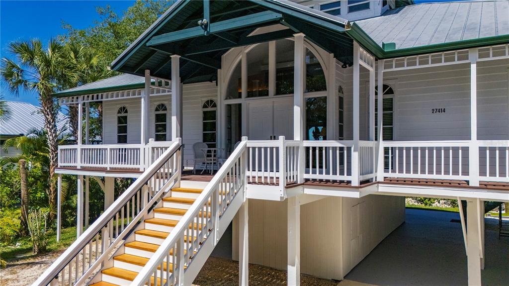 An elevated white house features a covered porch, wooden stairs, and a metal roof — 27414 MISTY AVENUE, PUNTA GORDA, FL