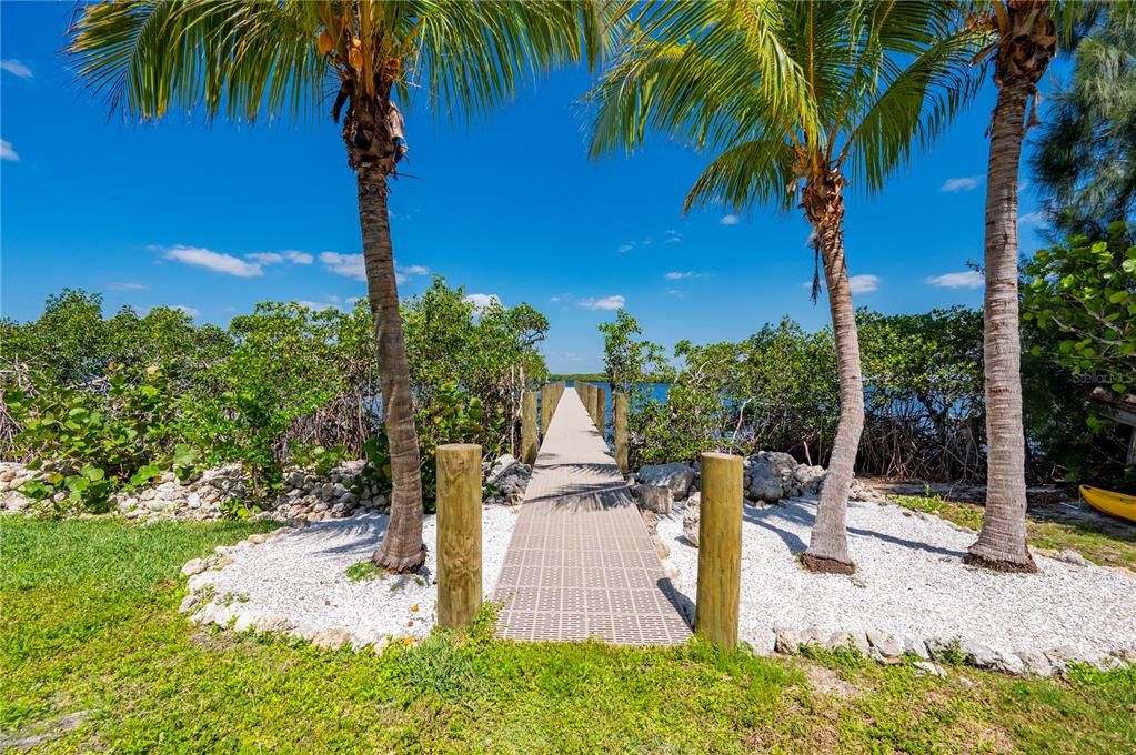 A wooden dock extends from a white gravel area between palm trees toward the water — 27414 MISTY AVENUE, PUNTA GORDA, FL