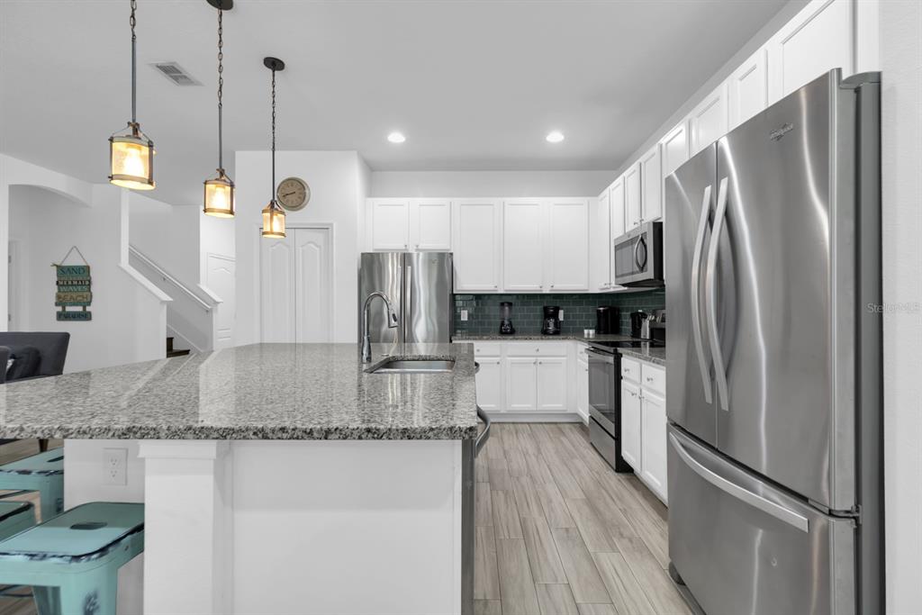 A modern kitchen features white cabinetry, granite countertops, stainless steel appliances, and wood-look flooring — 5248 OAKBOURNE AVENUE, DAVENPORT, FL