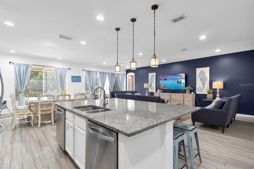 A kitchen island with granite countertops overlooks a living room with a dark blue wall — 5248 OAKBOURNE AVENUE, DAVENPORT, FL