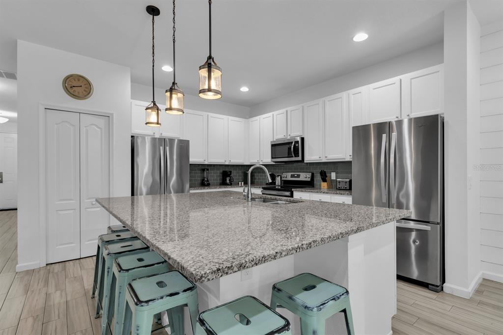 A kitchen features white cabinets, granite countertops, a large island, and stainless steel appliances — 5248 OAKBOURNE AVENUE, DAVENPORT, FL