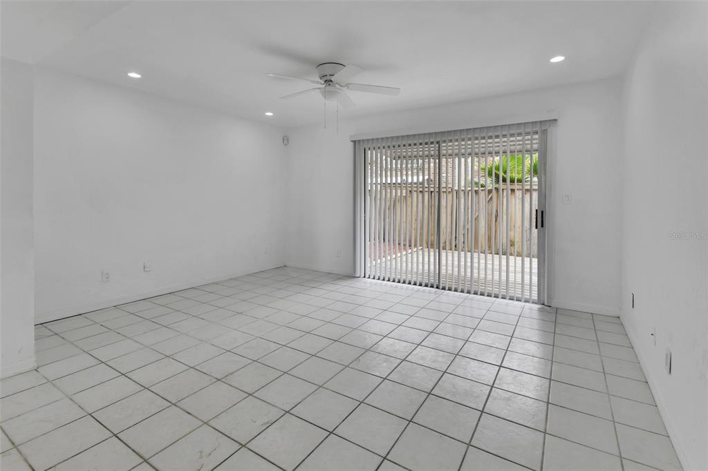 An empty room with white walls, white tile flooring, a ceiling fan, and sliding glass doors — 2200 S PALMETTO AVENUE UNIT A040, DAYTONA BEACH, FL