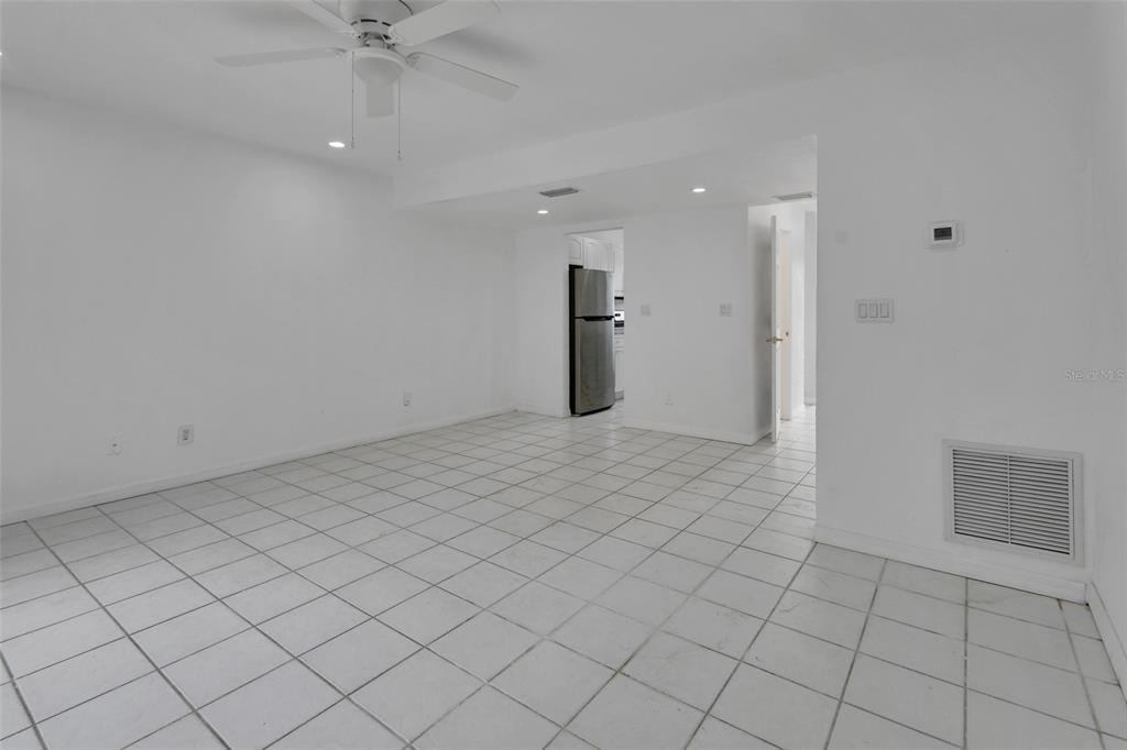 A white-walled room with white tiled flooring, a ceiling fan, and a doorway to a kitchen — 2200 S PALMETTO AVENUE UNIT A040, DAYTONA BEACH, FL