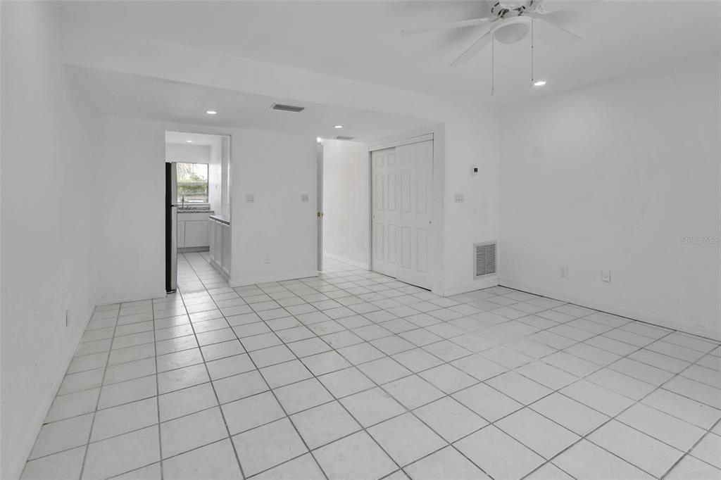 A bright, white-walled room with white tile flooring, a ceiling fan, and a kitchen doorway — 2200 S PALMETTO AVENUE UNIT A040, DAYTONA BEACH, FL