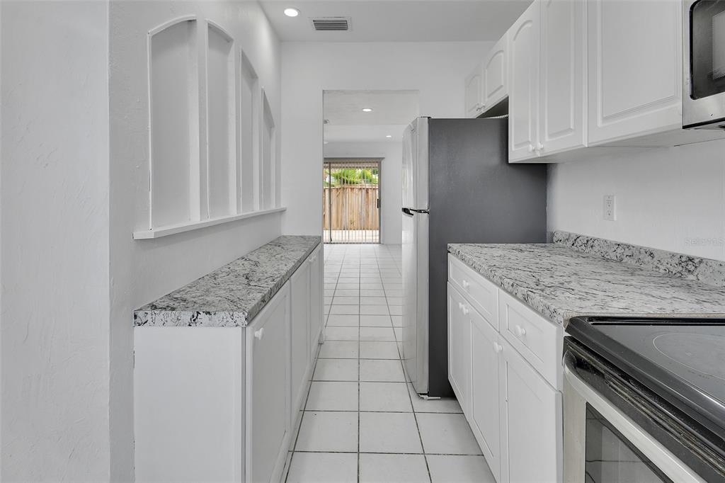 A galley kitchen features white cabinets, granite countertops, stainless steel appliances, and white tile flooring — 2200 S PALMETTO AVENUE UNIT A040, DAYTONA BEACH, FL