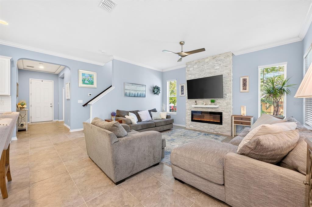 A living room features light blue walls, tile flooring, a stone fireplace, and gray furniture — 16936 TRADEWIND POINT, WINTER GARDEN, FL