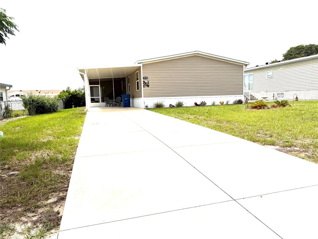 A single-story manufactured home features a tan exterior, a concrete driveway, and a screened-in porch — 9209 FONTAINE DRIVE, BROOKSVILLE, FL