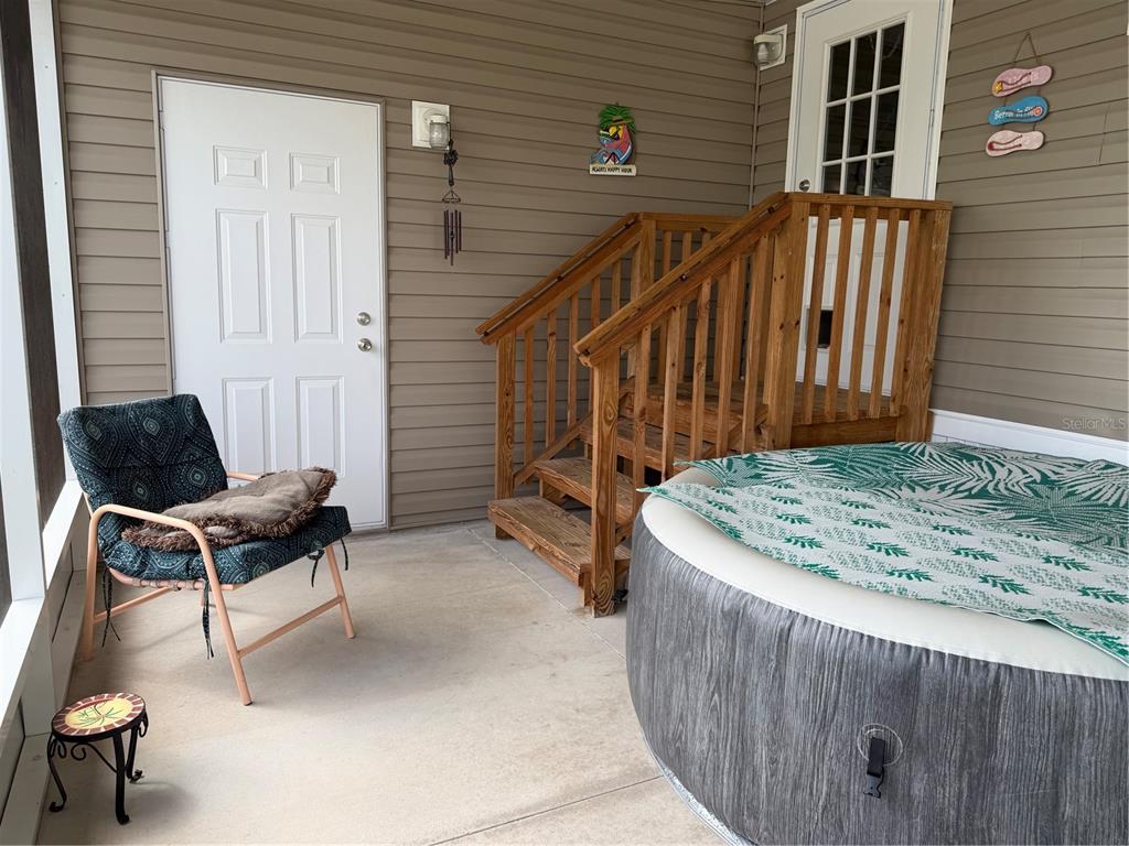 A screened-in porch features a hot tub, wooden stairs, a chair, and two exterior doors — 9209 FONTAINE DRIVE, BROOKSVILLE, FL