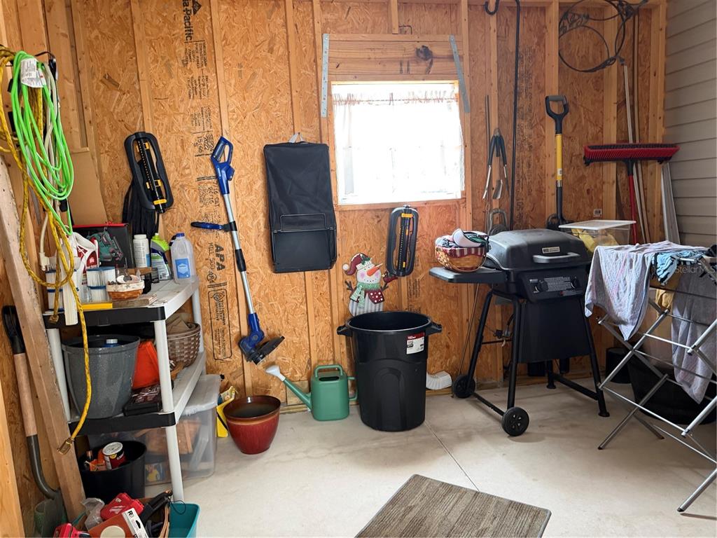 A storage shed interior features wood-paneled walls, a window, a grill, and various household items — 9209 FONTAINE DRIVE, BROOKSVILLE, FL