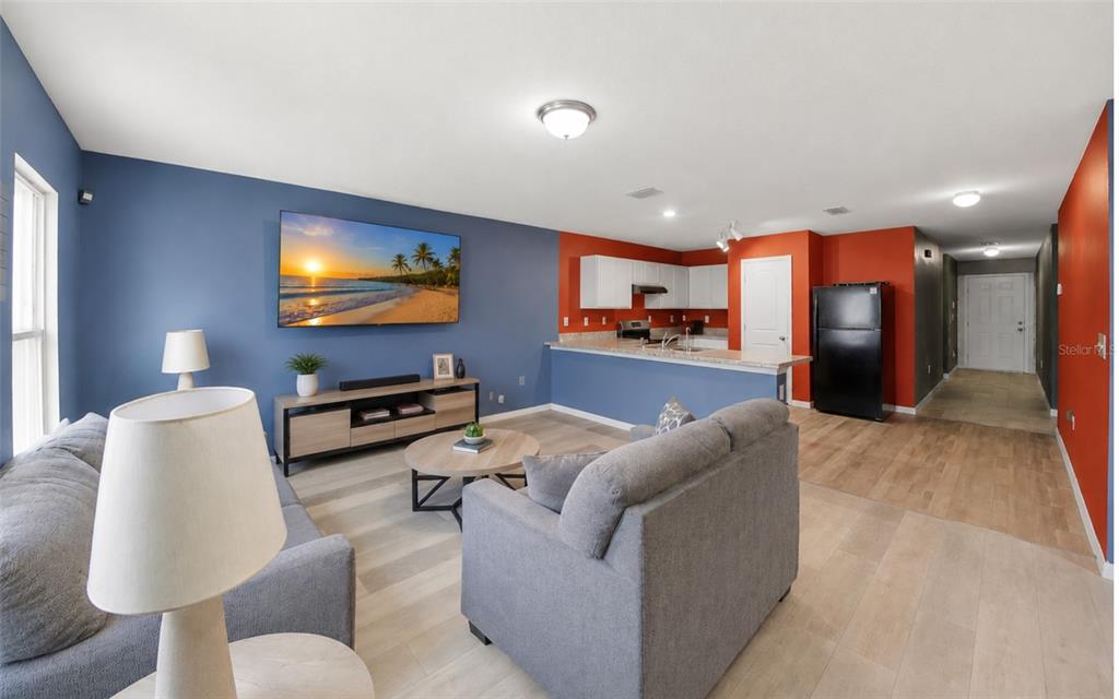 An open-concept living room and kitchen featuring blue and orange walls and light wood flooring — 280 FIG COURT, POINCIANA, FL