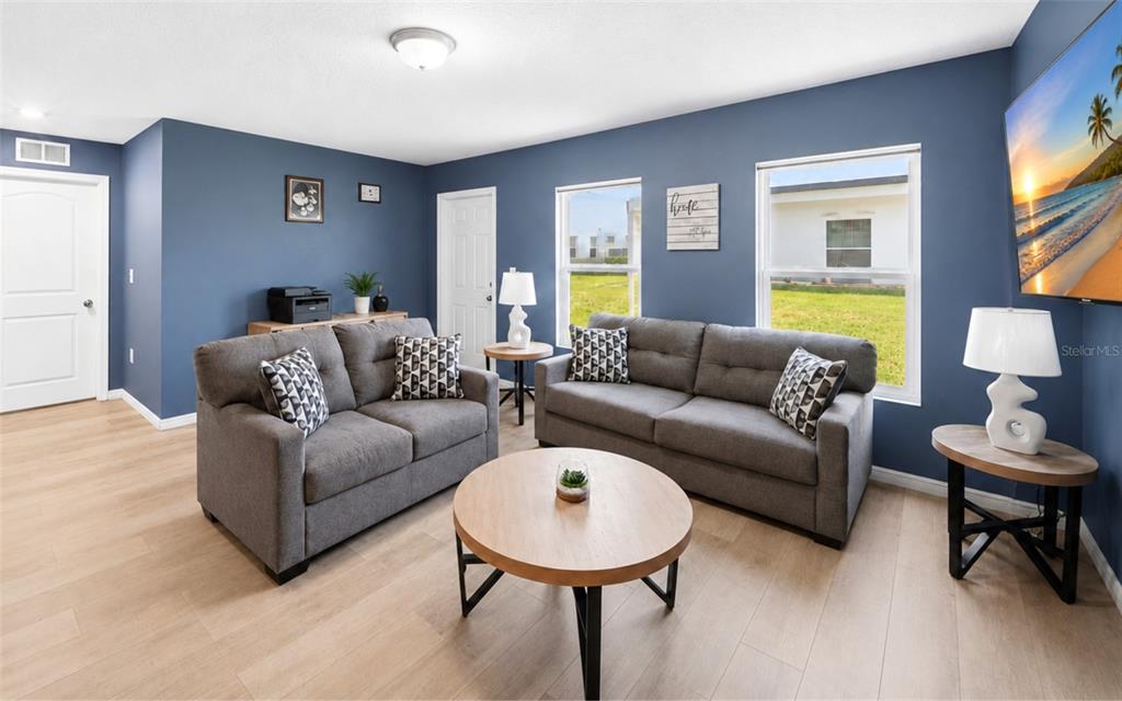 A living room with blue walls, two gray sofas, a round coffee table, and windows — 280 FIG COURT, POINCIANA, FL