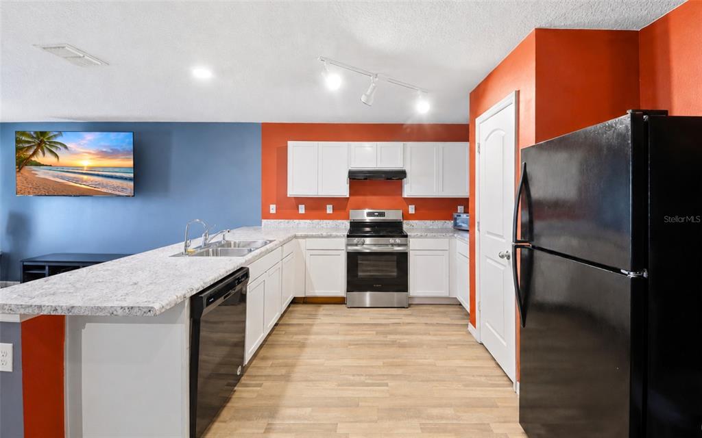 A kitchen features white cabinetry, stainless steel appliances, and a granite countertop breakfast bar — 280 FIG COURT, POINCIANA, FL