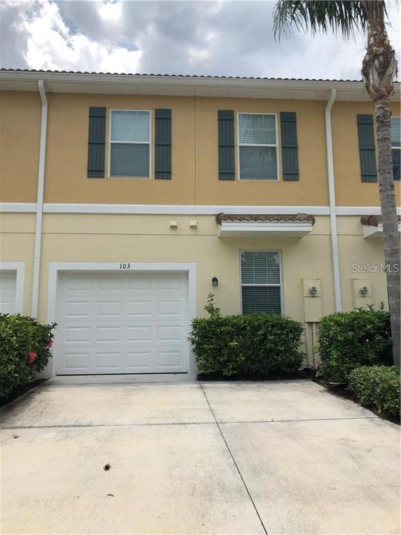 A two-story townhouse exterior with a white garage door, beige stucco walls, and green landscaping — 3770 82ND AVENUE CIRCLE E UNIT 103, SARASOTA, FL