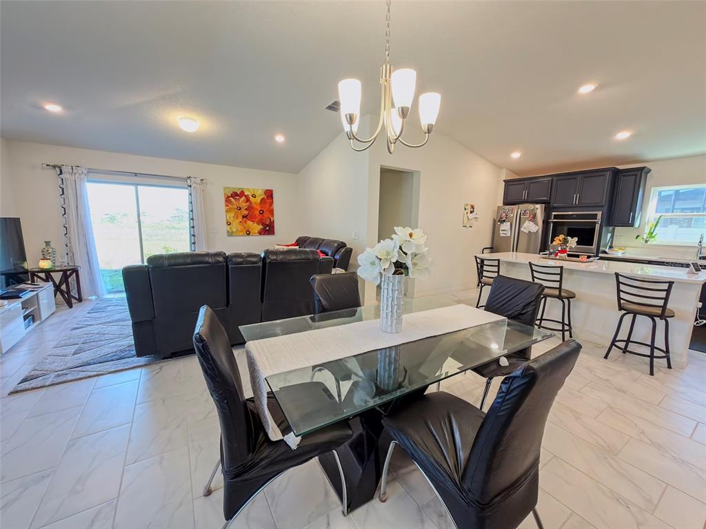 An open-concept dining area features a glass table, black chairs, and an adjacent kitchen — 334 PRESERVE POINTE BOULEVARD, DAVENPORT, FL