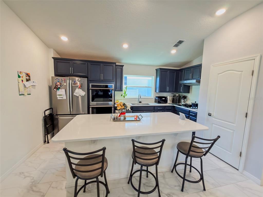 A kitchen features dark blue cabinets, a white quartz island, and stainless steel appliances — 334 PRESERVE POINTE BOULEVARD, DAVENPORT, FL
