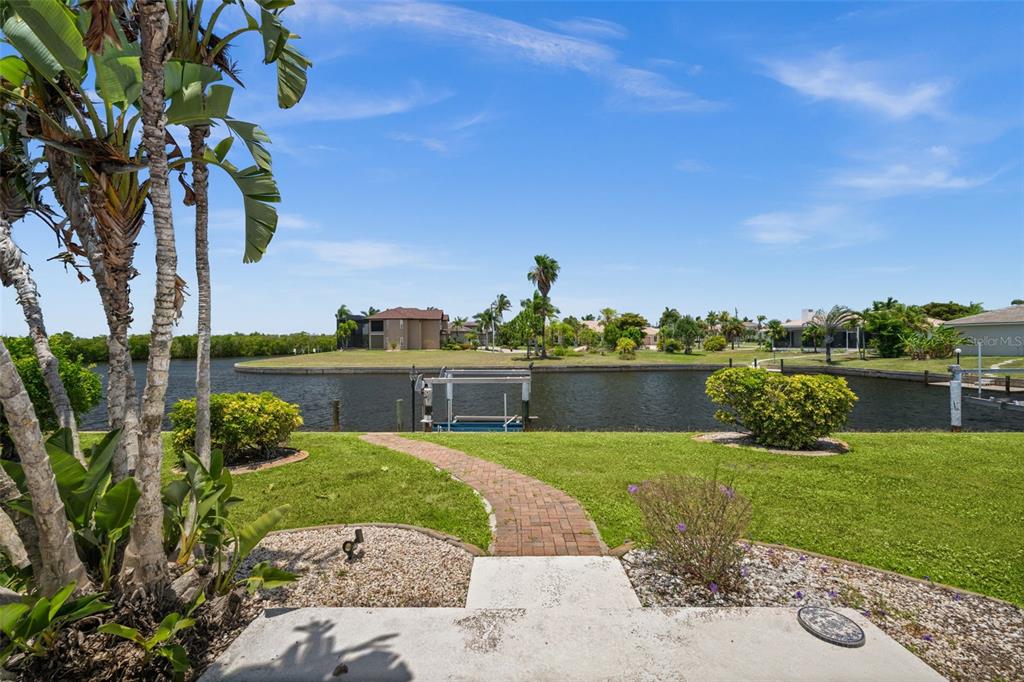 A brick walkway leads through a grassy backyard toward a canal with a boat lift — 3330 TRIPOLI BOULEVARD, PUNTA GORDA, FL