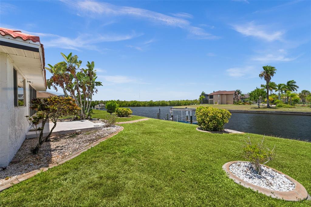 A view of a grassy backyard with a canal, boat dock, and tropical landscaping — 3330 TRIPOLI BOULEVARD, PUNTA GORDA, FL