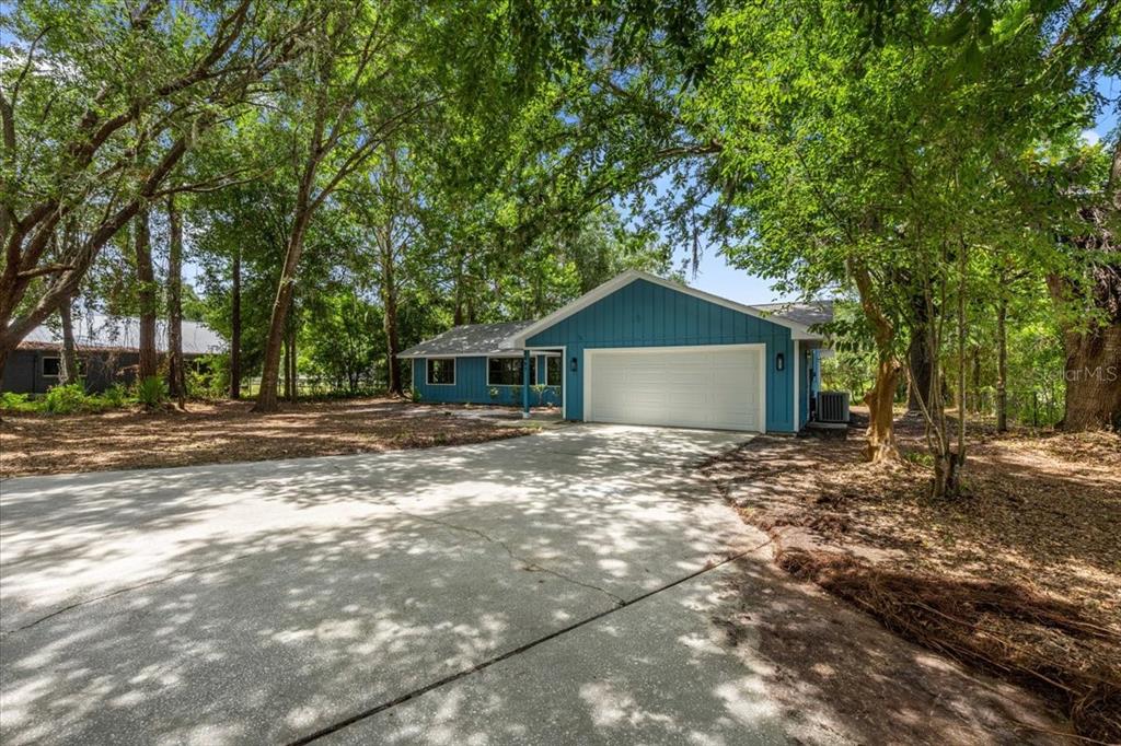 A blue single-story house with a white garage door sits on a wooded lot — 2907 S SKYLINE DRIVE, INVERNESS, FL