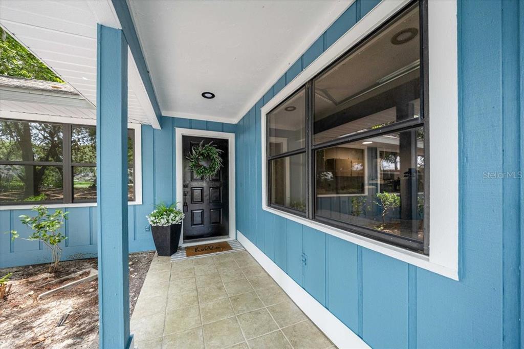 A covered front porch with blue vertical siding, a black front door, and tiled flooring — 2907 S SKYLINE DRIVE, INVERNESS, FL
