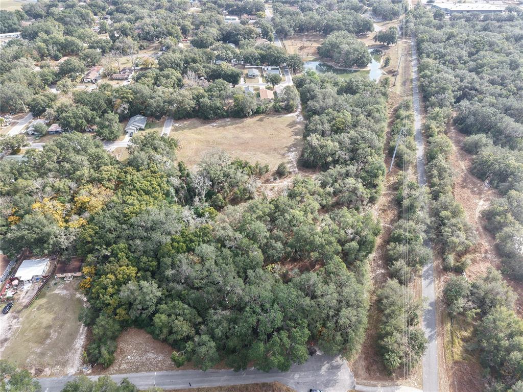 An aerial view shows a wooded lot with a cleared field and a nearby road — STINSON STREET, LEESBURG, FL