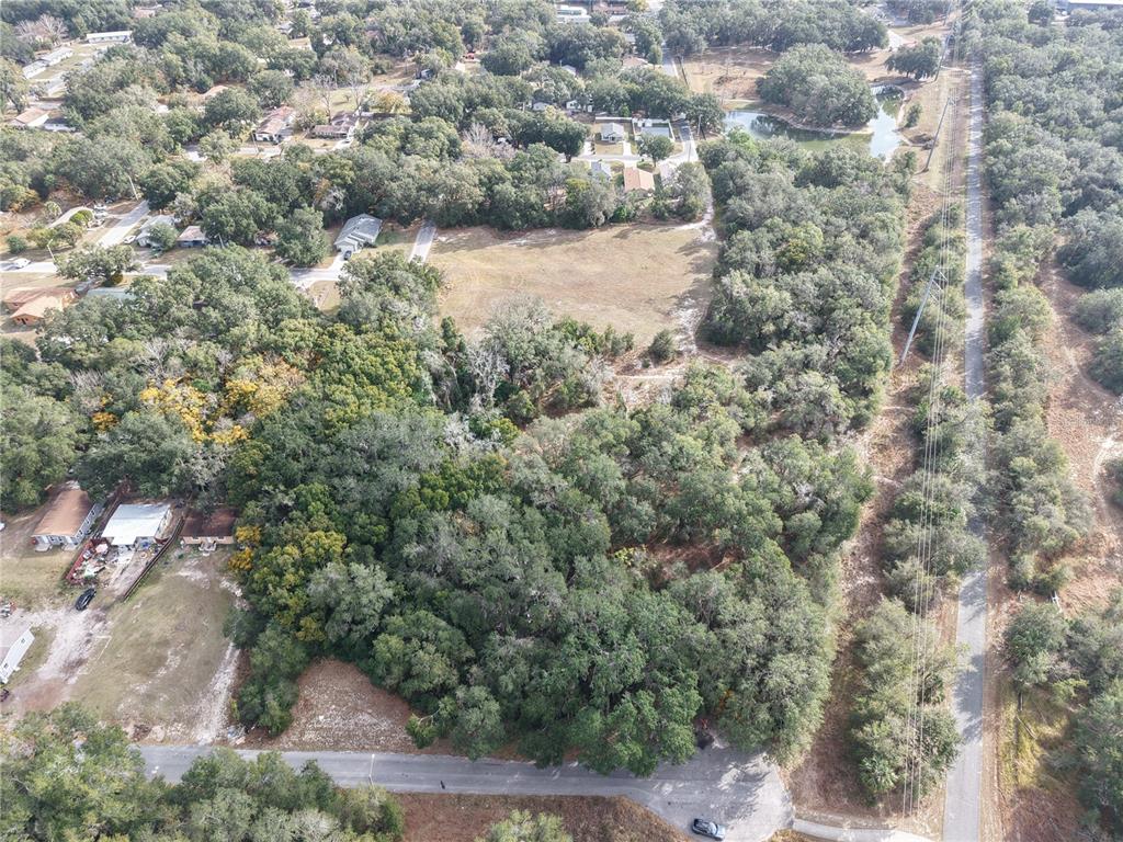 An aerial view shows a wooded lot with a cleared area and nearby residential houses — STINSON STREET, LEESBURG, FL