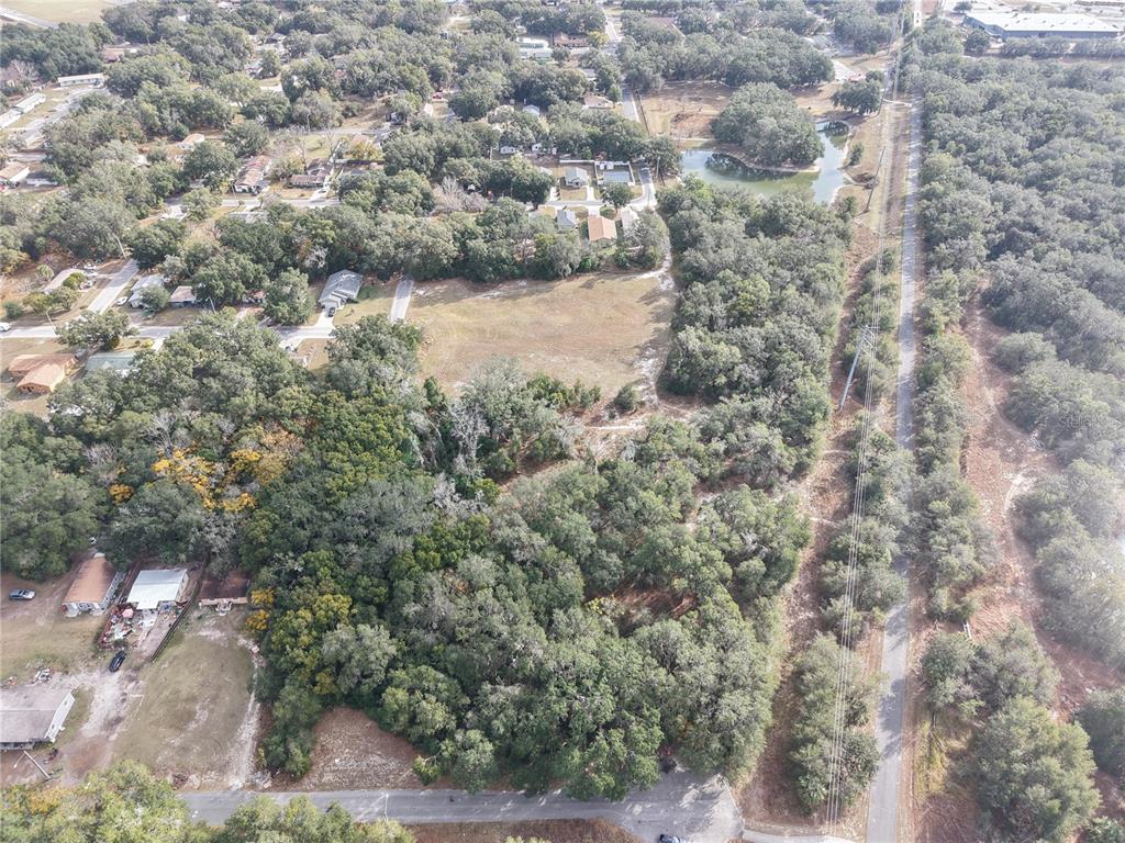 An aerial view shows a large, partially wooded plot of land with a small pond — STINSON STREET, LEESBURG, FL