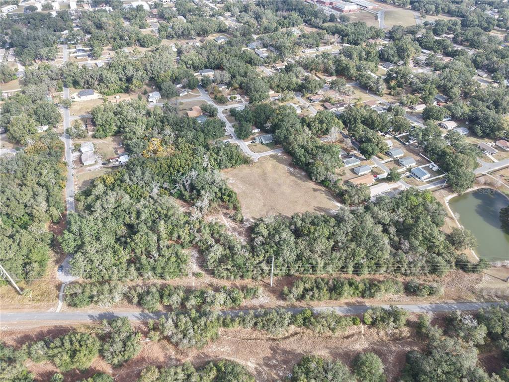 An aerial view shows a vacant, grassy lot surrounded by trees and residential houses — STINSON STREET, LEESBURG, FL
