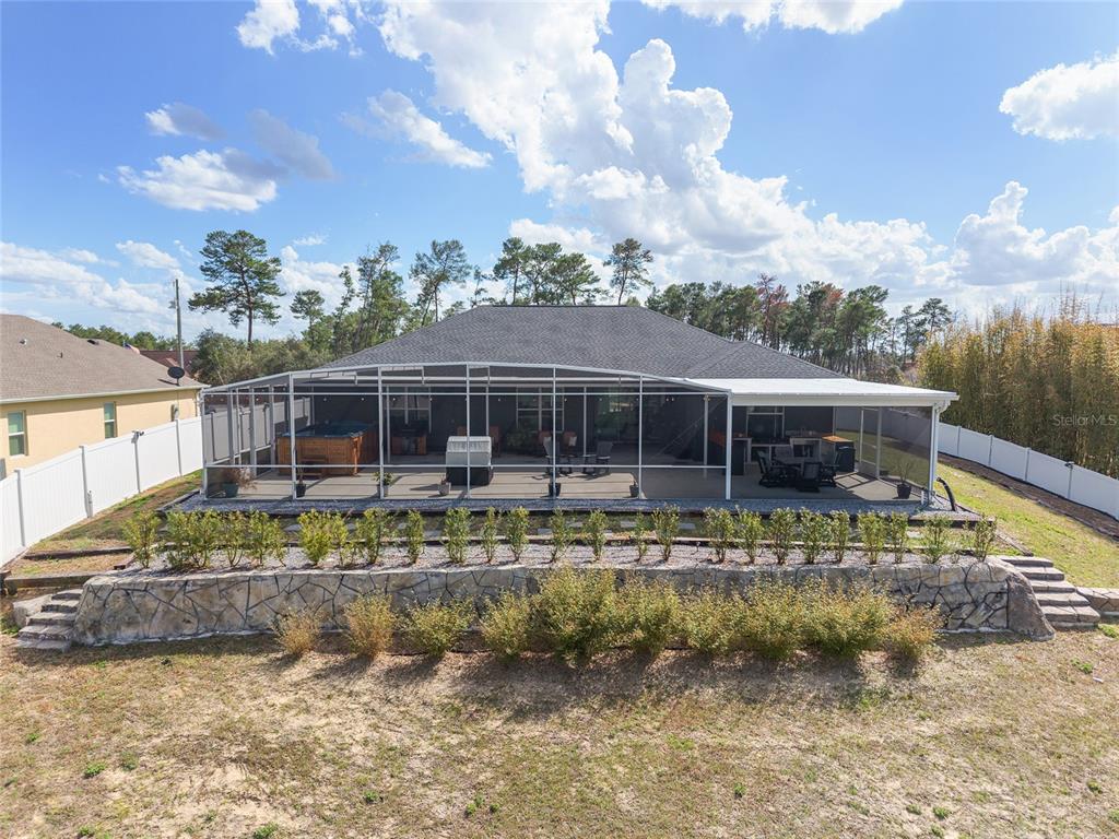 A rear view of a house with a screened-in patio, hot tub, and stone retaining wall — 4321 SW 106TH PLACE, OCALA, FL