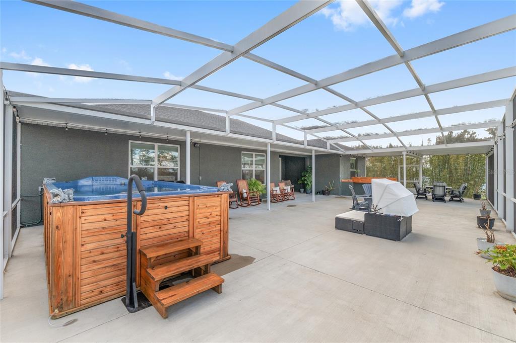 A screened-in concrete patio features a wooden hot tub, outdoor furniture, and a covered area — 4321 SW 106TH PLACE, OCALA, FL