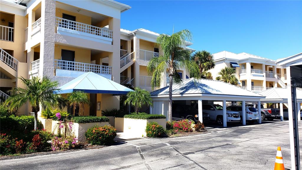 A multi-story apartment complex features covered parking, palm trees, and balconies under a clear sky — 2424 PLACIDA ROAD UNIT C104, ENGLEWOOD, FL