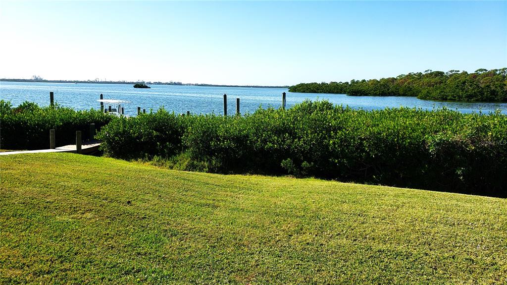 A grassy lawn leads to a wooden dock overlooking a bay with dense shoreline vegetation — 2424 PLACIDA ROAD UNIT C104, ENGLEWOOD, FL