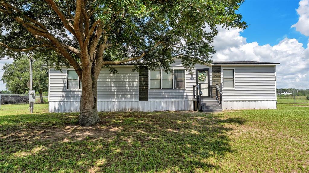 A single-story manufactured home with light gray siding and a large tree in front — 1329 ASHLEE COURT, AUBURNDALE, FL