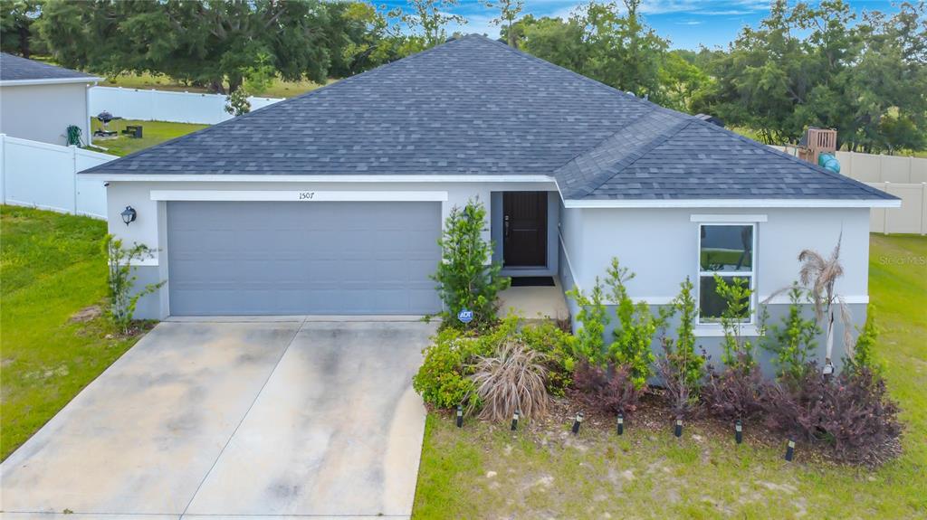 A single-story house with a gray garage, dark roof, and front landscaping — 1507 GERANIUM DRIVE, MASCOTTE, FL