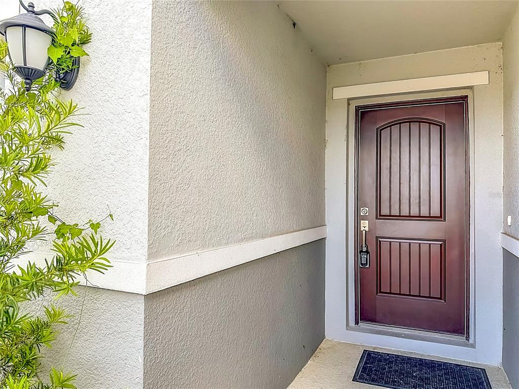 A dark brown front door with a keypad lock sits under a covered entryway — 1507 GERANIUM DRIVE, MASCOTTE, FL